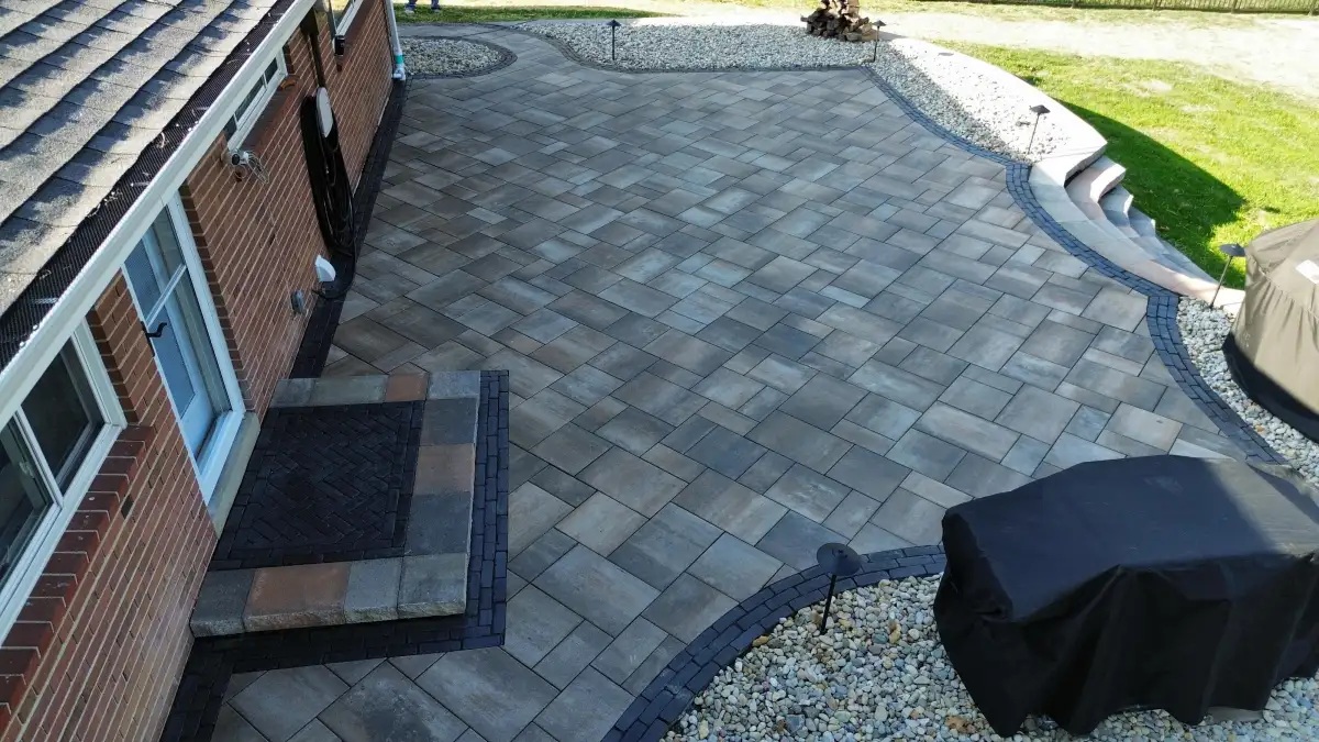 Large paver patio with fire pit area and curved border by Green Operations