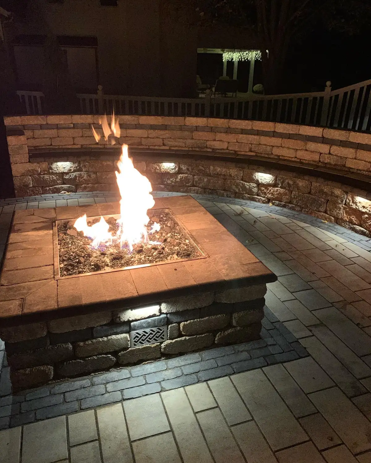 Fire pit with seating wall lit up at night in St. Louis backyard